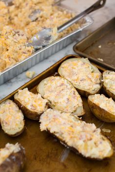 baked potatoes with cheese and other toppings in pans on a table next to baking sheet