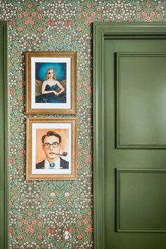 two framed pictures hang on the wall in front of green painted doors and floral wallpaper