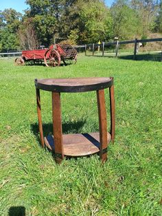 an old wooden table sitting in the middle of a grass field next to a red wagon