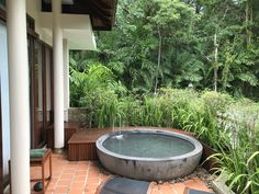 an outdoor hot tub sitting on top of a brick patio next to a lush green forest