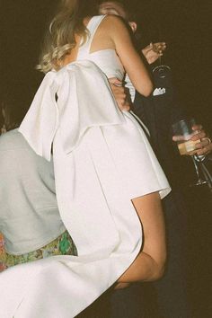 a woman in a white dress is hugging another woman's back at a party