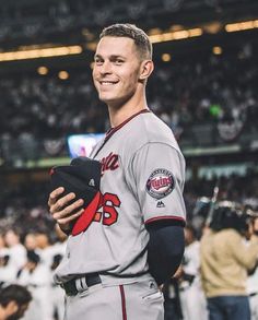 a baseball player standing in the middle of a stadium holding a hat and smiling at the camera