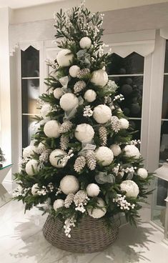 a christmas tree decorated with white balls and greenery in a basket on the floor