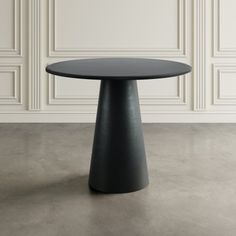 a black round table sitting on top of a cement floor next to a white wall