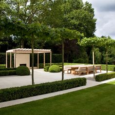 an outdoor area with benches and trees in the middle, surrounded by hedges on both sides