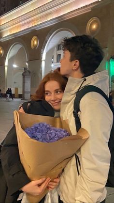 a man holding a bouquet of purple flowers next to a woman in a white shirt