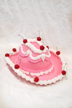 a pink cake with white frosting and cherries sitting on top of a table