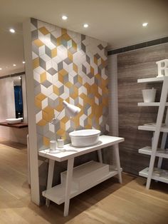 a white table with a bowl on it in front of a wall that has yellow and grey tiles