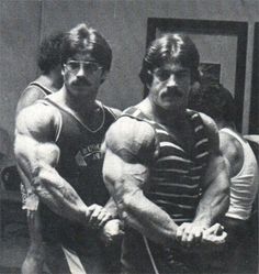 two men standing next to each other in front of a mirror with their arms crossed