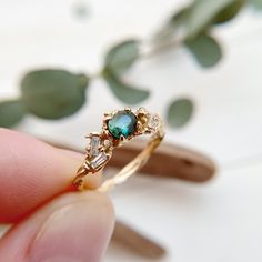 a person is holding a ring with two stones on it and green leaves in the background