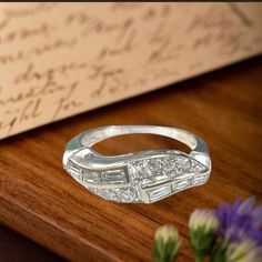 a silver ring sitting on top of a wooden table next to flowers and an envelope