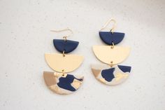 two tone drop earrings with gold and blue accents on white marbled surface, hanging from brass earwires