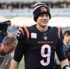 a football player wearing a black jersey and a beanie walks on the sidelines