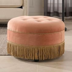 a round ottoman with tassels on it in front of a couch and rug