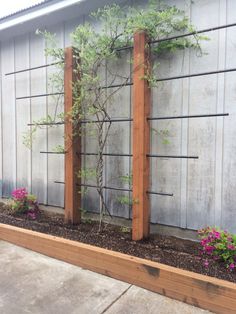 a wooden planter filled with plants next to a wall and cement slabs on the ground