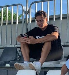 a man sitting on the bleachers looking at his cell phone while another person sits behind him