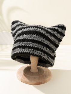 a crocheted cat hat sitting on top of a wooden head stand in front of a white wall