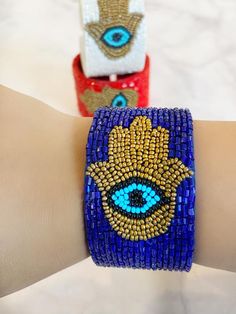 All the vibes you need to keep the evil away in one bracelet. A intricate Hamsa and a bold evil eye design crafted into a luxurious chic  bracelet.  Always protected!! Timeless enough to be worn with any outfit. Slides on and off with an open cuff flexible enough to fit everyone.Comes in sleek FRESHALAMODE packaging making it perfect for gifting. A hamsa prayer card is included as well. Choose between 3 rich colors. RedWhite Blue Handmade Symbolic Beaded Bangle Bracelets, Handmade Symbolic Beaded Bangle Bracelet, Handmade Symbolic Cuff Bracelet For Festivals, Symbolic Handmade Bracelets For Festivals, Spiritual Beaded Cuff Bracelet Gift, Spiritual Beaded Wristband Bangle, Bohemian Evil Eye Jewelry For Party, Bohemian Blue Cuff Bracelet For Party, Bohemian Bangle Stretch Bracelet For Party