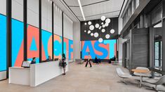 people are walking through the lobby of an office building with large colorful letters on the wall