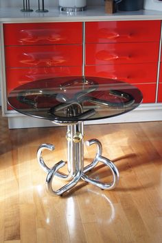 a glass table with metal legs on a wooden floor in front of red cabinets and drawers