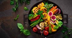 a skillet filled with vegetables on top of a table next to herbs and spices