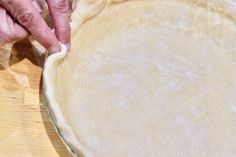 an older person is making a pie crust on a wooden table with a knife and fork