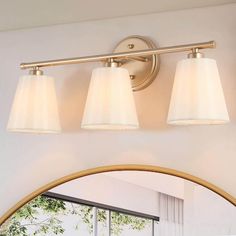 three light bathroom fixture with white shades on the glass and gold trim around the lights