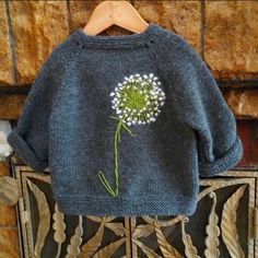 a blue sweater with a dandelion on it hanging from a wooden hanger