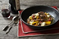 a bowl filled with meat and vegetables on top of a red napkin next to a bottle of wine