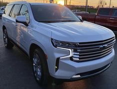 a white suv parked in a parking lot with other cars and trucks behind it at sunset