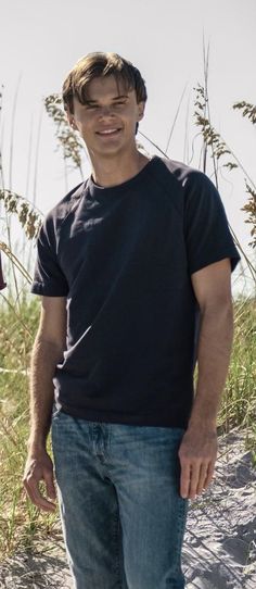 a man is standing on the beach with his hands in his pockets and smiling at the camera