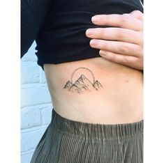 a woman's stomach with a mountain tattoo on her left side ribcage