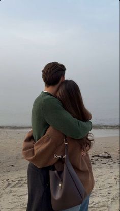 a man and woman hug on the beach while looking out at the ocean from behind them