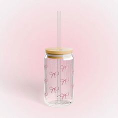 a glass jar with a straw in it and pink bows on the lid, against a light pink background