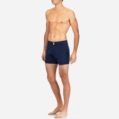 a man standing in front of a white background wearing navy blue swim trunks and no shirt