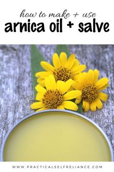 two yellow flowers sitting on top of a wooden table next to a jar of oil