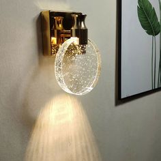 a light that is on the wall next to a plant in a room with white walls