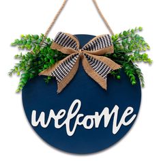 a welcome sign hanging on the side of a wall with a bow and greenery