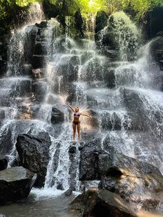 a woman standing in front of a waterfall with her arms up and hands raised above her head