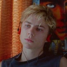 a young man wearing headphones in front of a window with an orange curtain behind him