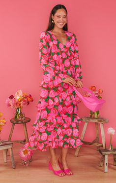 a woman standing in front of a pink wall wearing a long dress with flowers on it