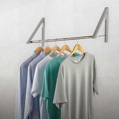 four shirts hanging on a clothes rack in front of a white wall and two wooden hangers