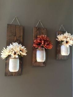 three mason jars with flowers hanging on the wall