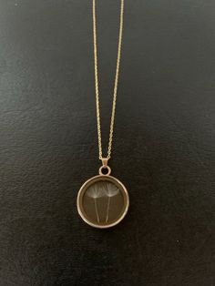 a necklace with a dandelion in the center on a black surface, hanging from a gold chain