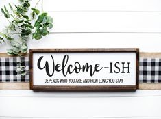 a welcome sign hanging on the side of a white wall next to a potted plant