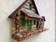 a wooden birdhouse with green windows on the side of a building, made out of wood