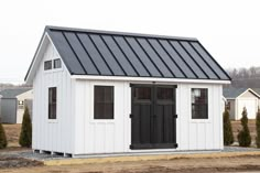 a small white shed with a black door and windows on the roof is shown in front of some houses