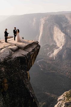 the bride and groom are standing at the edge of a cliff looking out into the valley