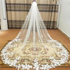 a white wedding veil with flowers on the floor in front of a curtained window