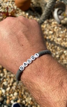 a man wearing a bracelet with the word beaded on it's wrist, in front of some rocks